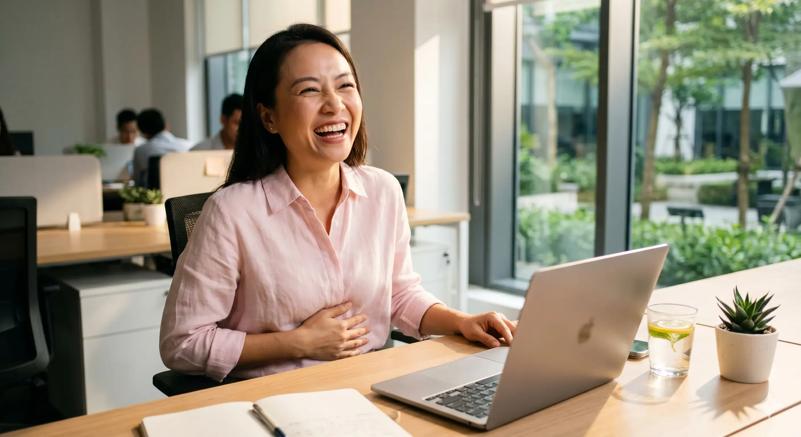 Người phụ nữ cười vui vẻ tại bàn làm việc - lợi ích của tiếng cười đối với sức khỏe